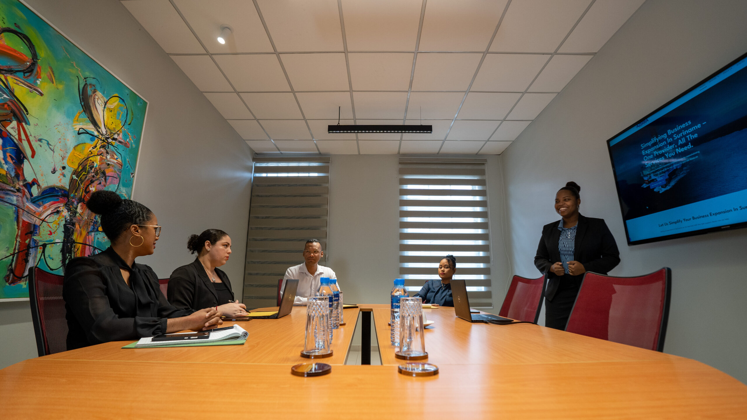 Business meeting in a conference room with five people and a presentation screen.
