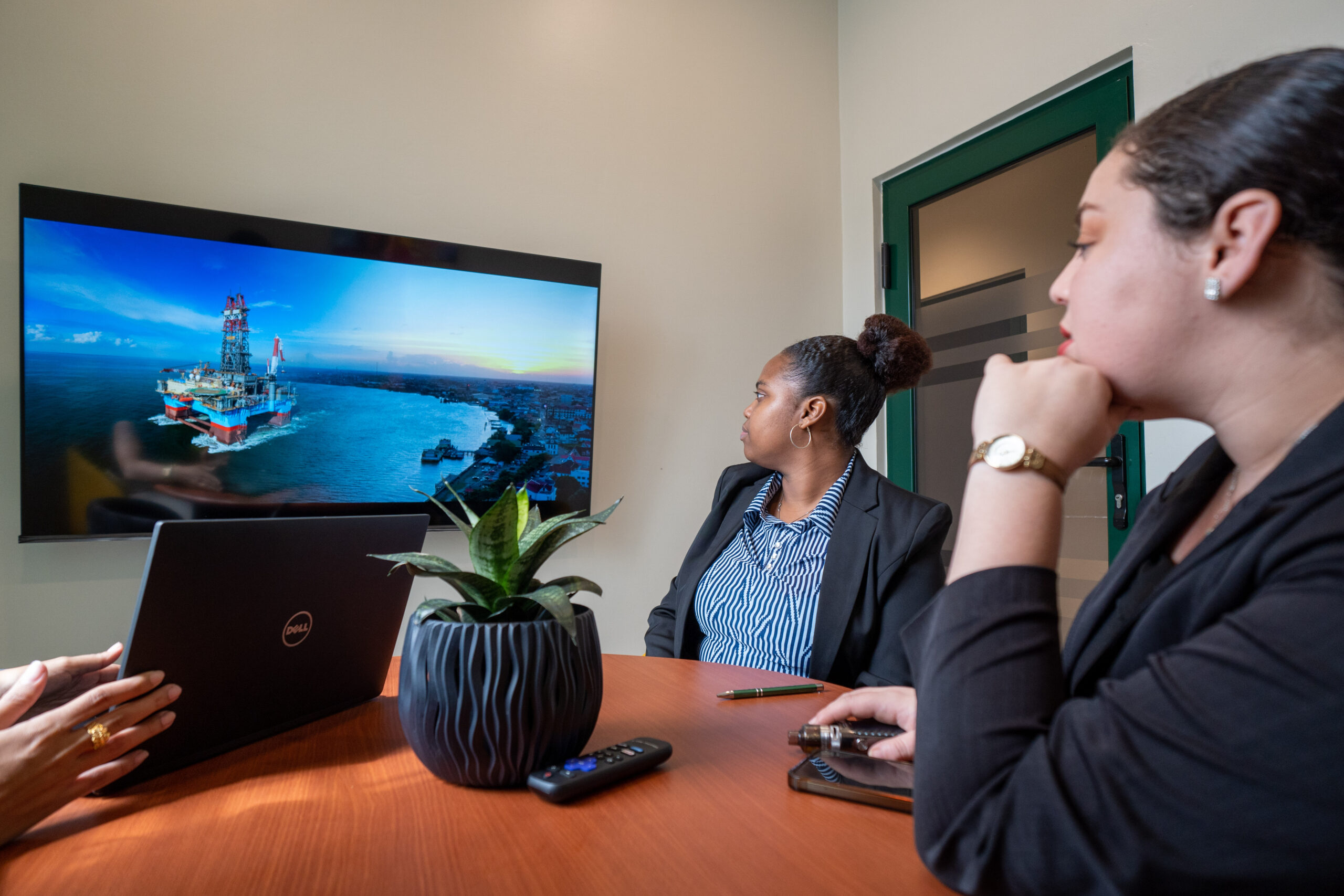 Two businesswomen watching a presentation on a wall-mounted screen in a meeting room