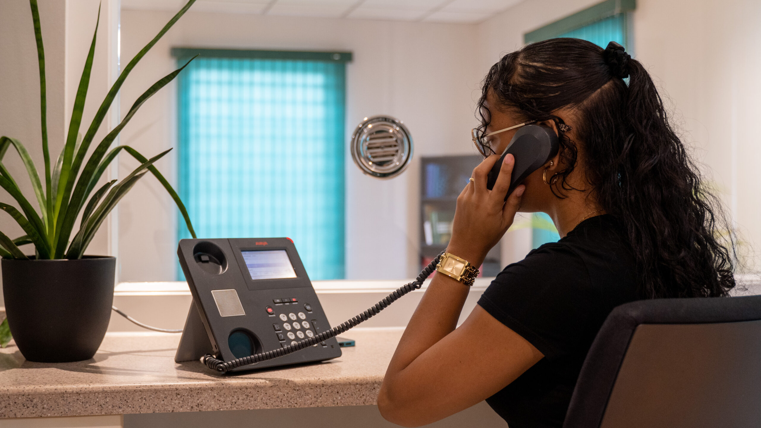 Woman talking on a landline phone at an office reception desk.