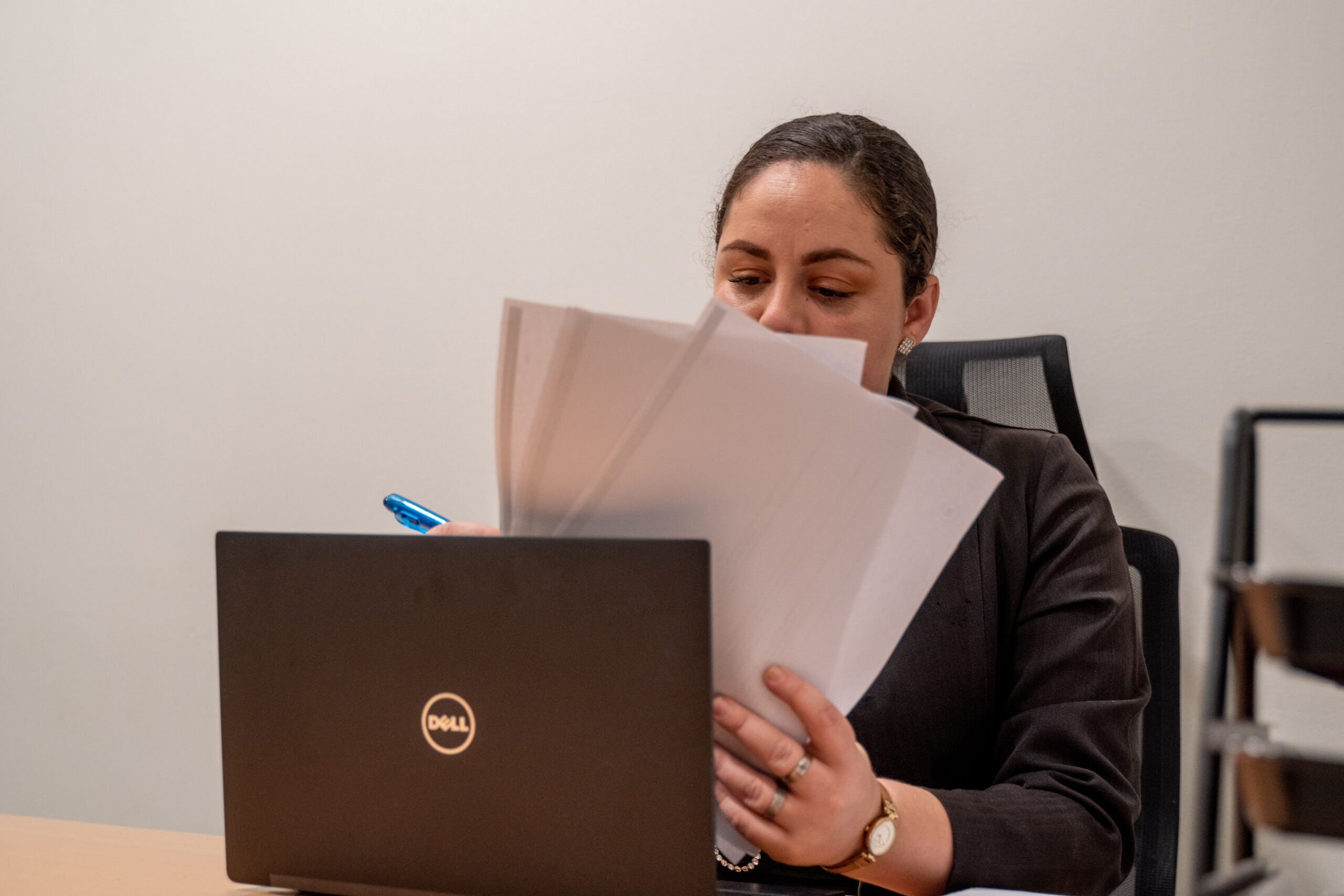 Woman reviewing documents while working on a laptop at her desk.